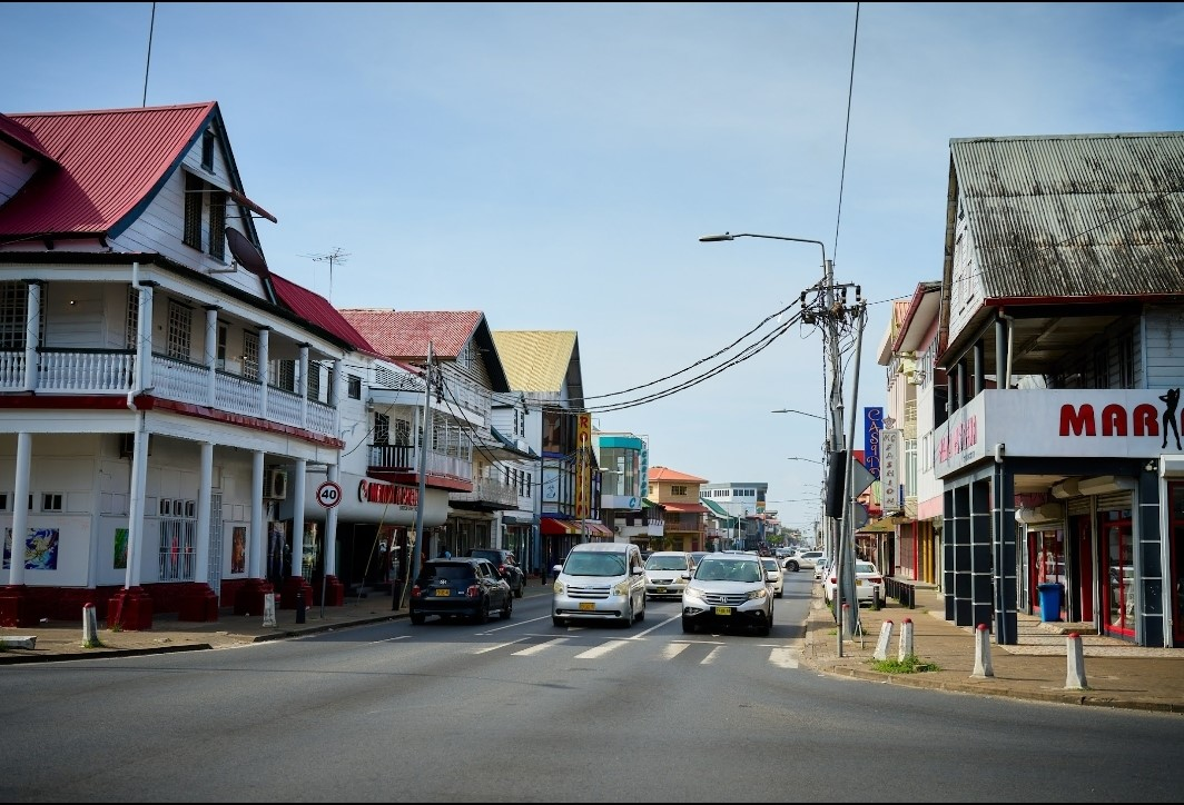Straat in Paramaribo, Suriname — houten koloniale huizen met rode daken, auto's en levendige winkels