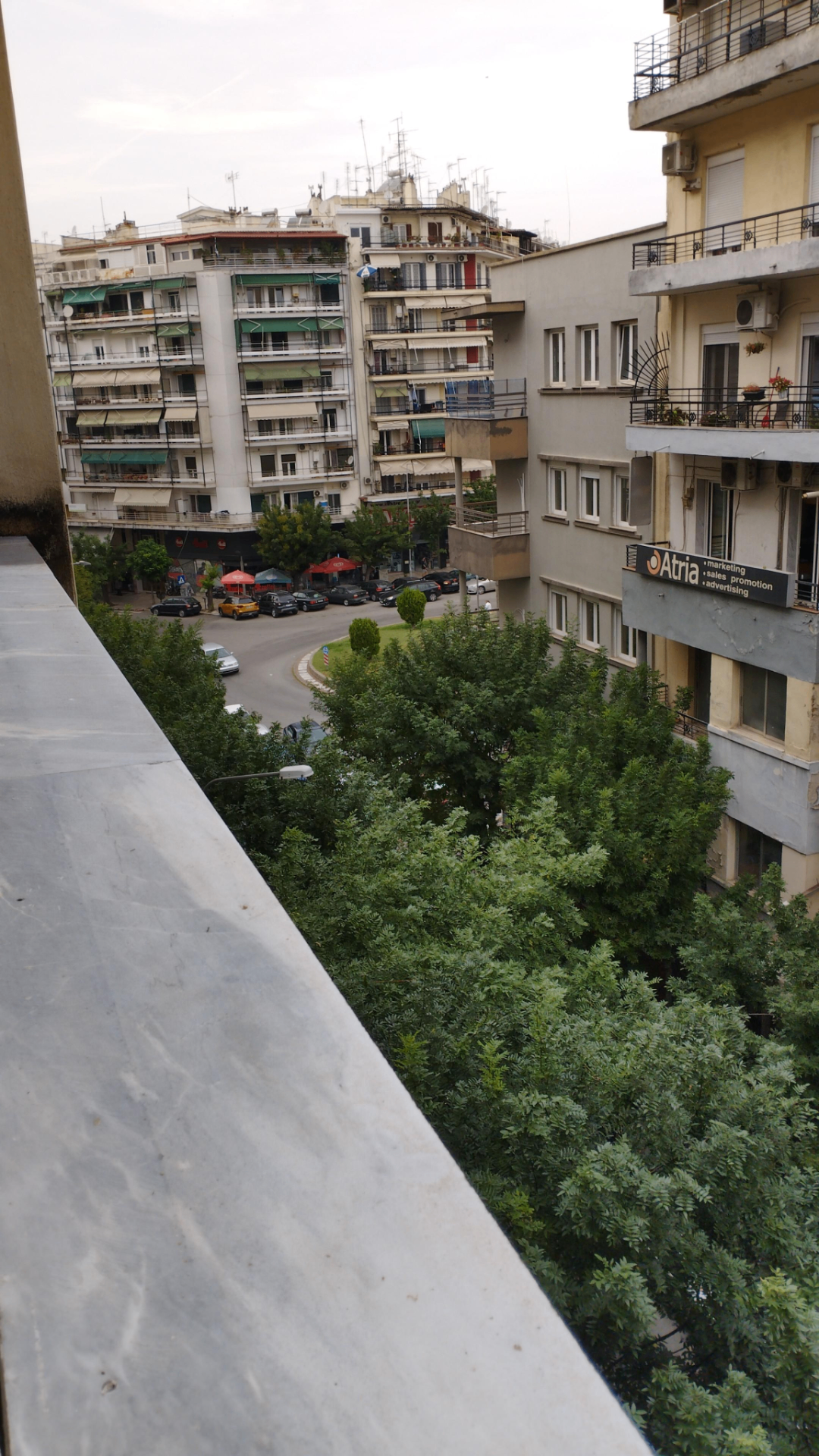 Uitzicht vanaf een balkon in Thessaloniki op een authentiek Grieks straatje met appartementencomplexen en groene bomen