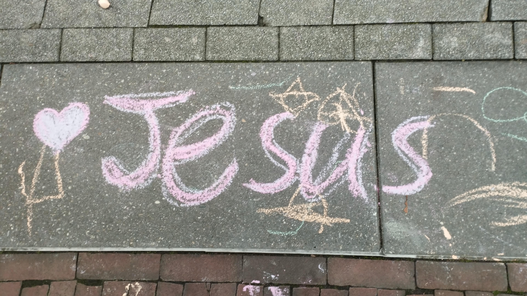 Met krijt op straat geschreven: hart Jesus in roze letters met een kroon